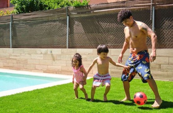 Veja como usar grama sintética na piscina com a Stampa Gramas! Família brinca com bola sobre o revestimento de grama sintética na piscina.