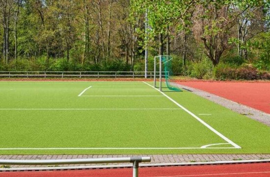 Saiba quando usar grama sintética para quadras poliesportivas! Campo verde com trave e rede ilustra a grama sintética para quadra poliesportiva.