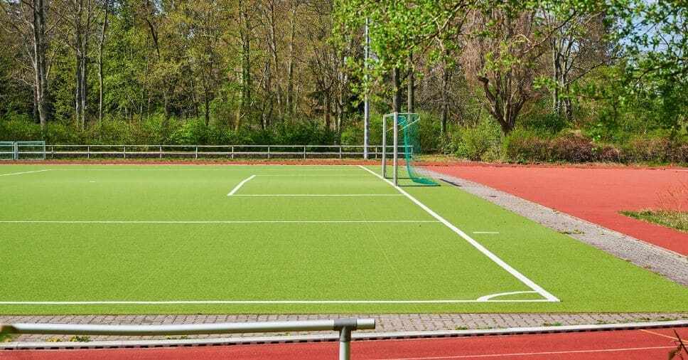 Campo verde com trave e rede ilustra a grama sintética para quadra poliesportiva.